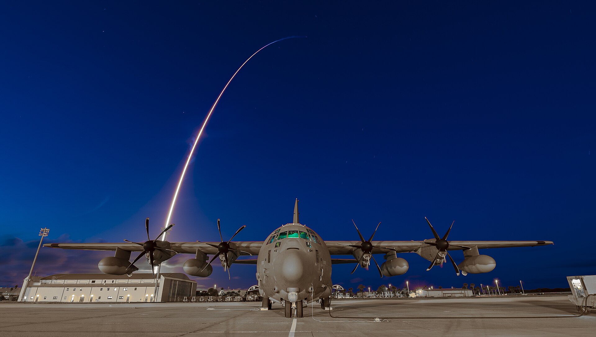 A rescue aircraft on the Patrick Space Force Base flight line as a rocket launches in the background.